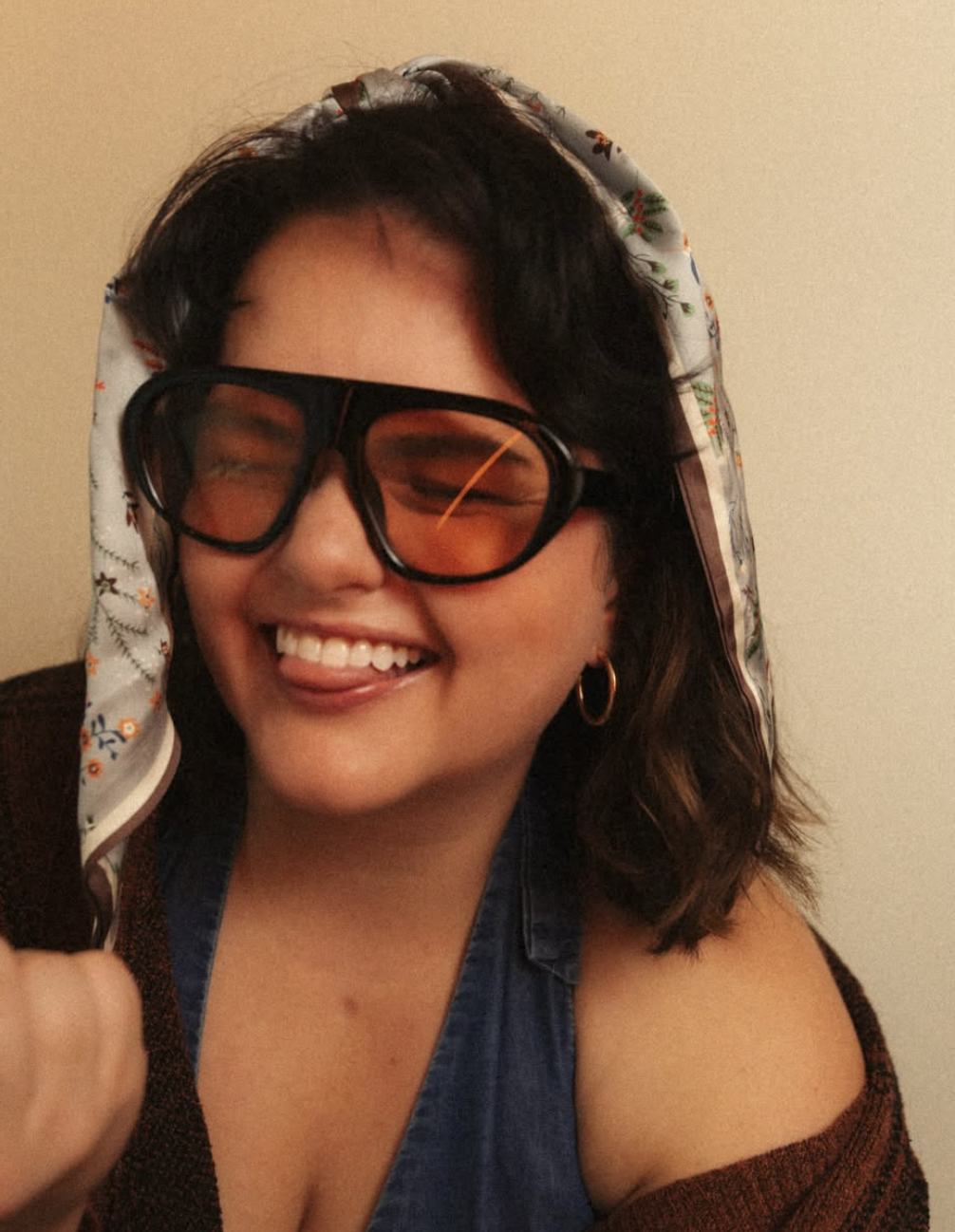 A woman laughing in oversized aviators and a printed headscarf